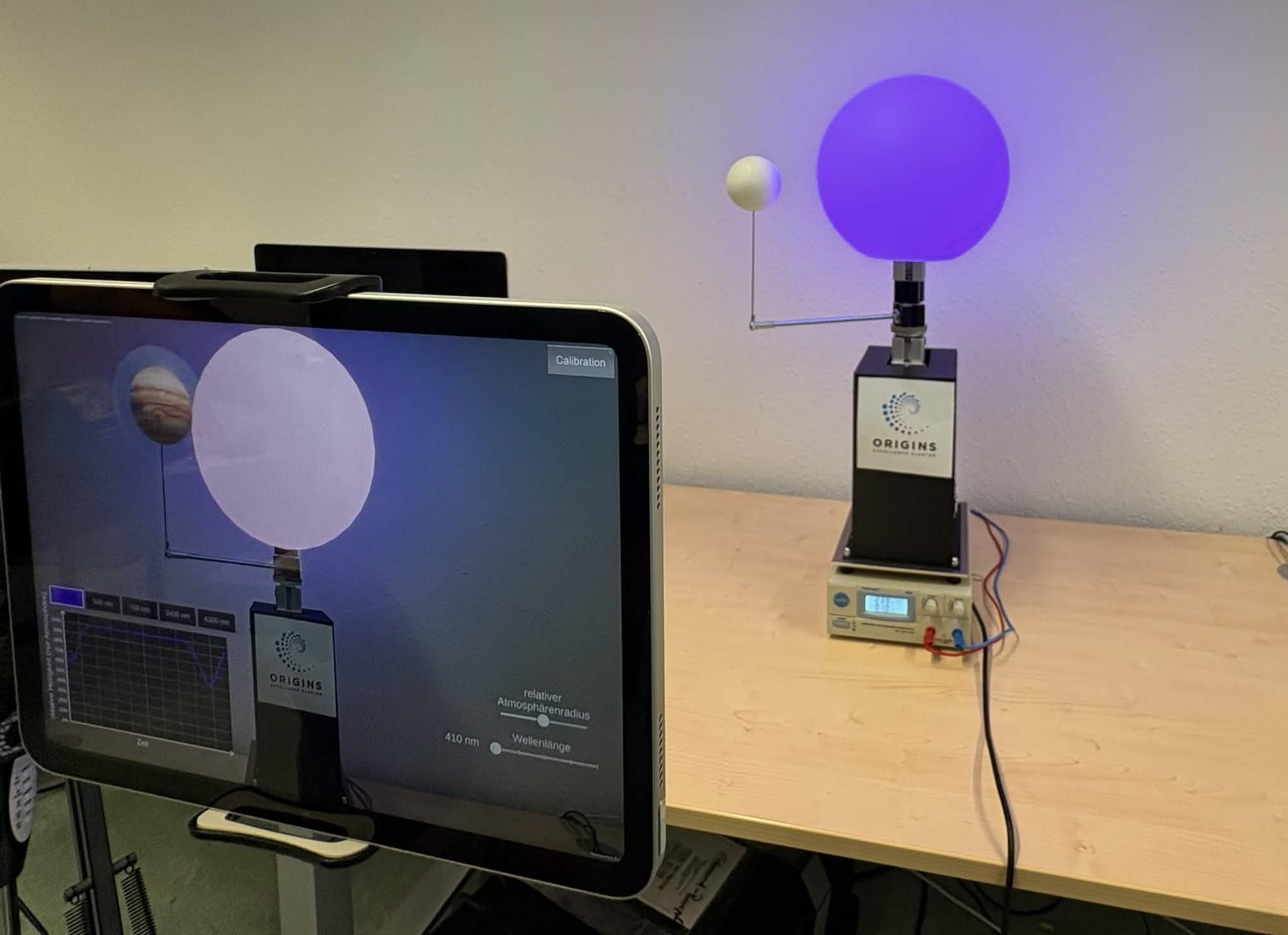 Motorized model of a glowing star and orbiting planet beside an iPad running the AR app